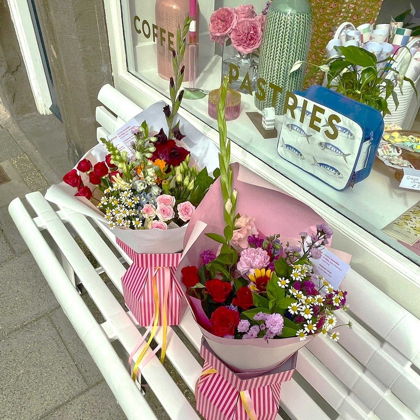 Two flower bouquets on a white bench with a shopfront in the background.