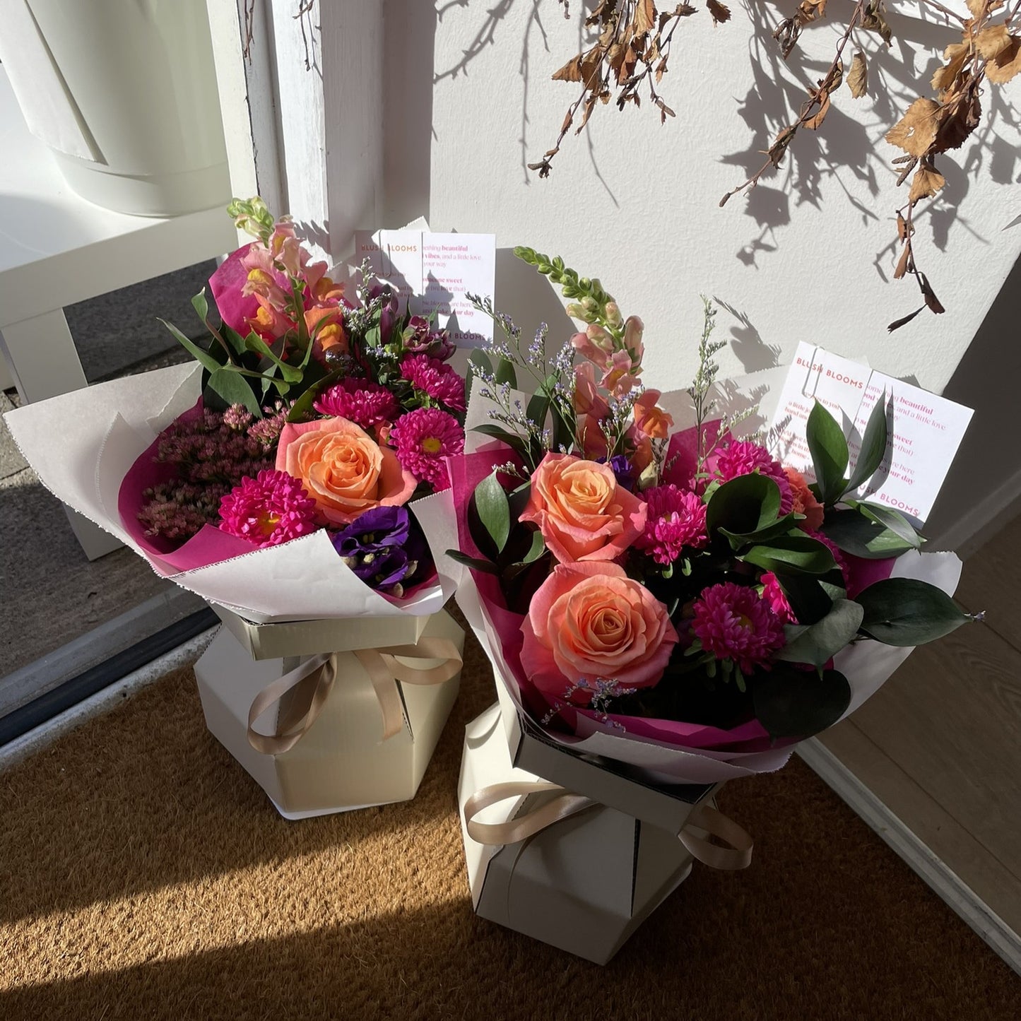 Two bouquets of flowers on a carpeted floor with a neutral wall in the background.