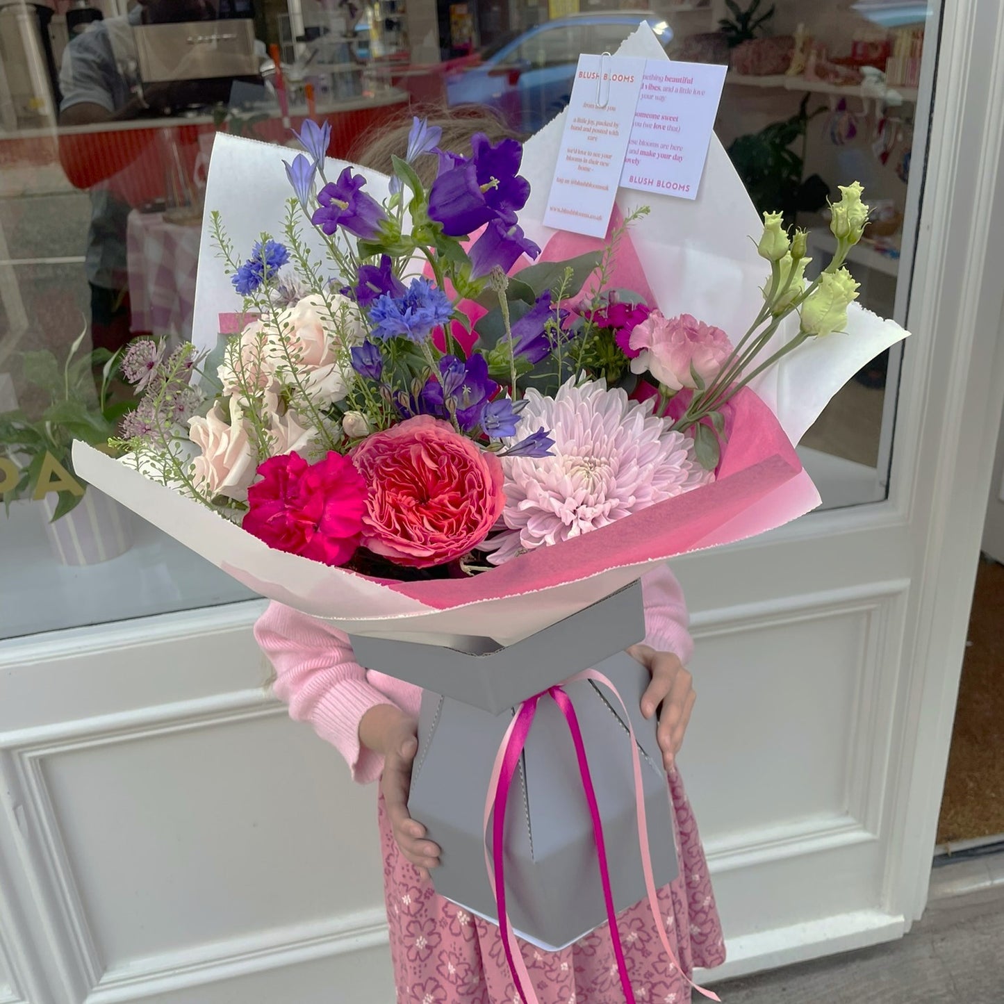 Bouquet of flowers held by a person in a pink outfit, with a blurred indoor background.