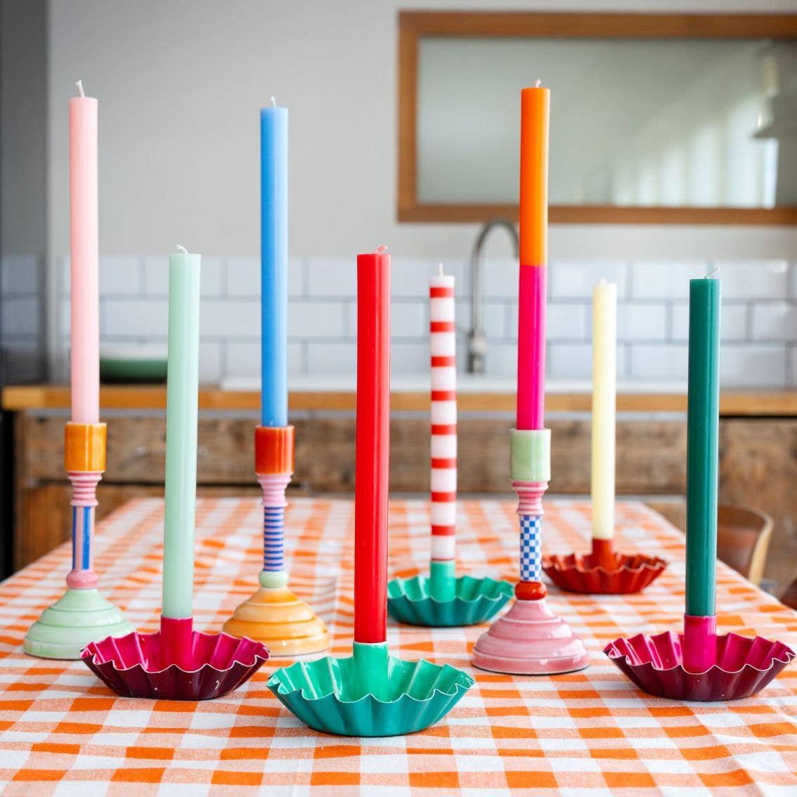 Colorful candles in various holders on a checkered tablecloth.