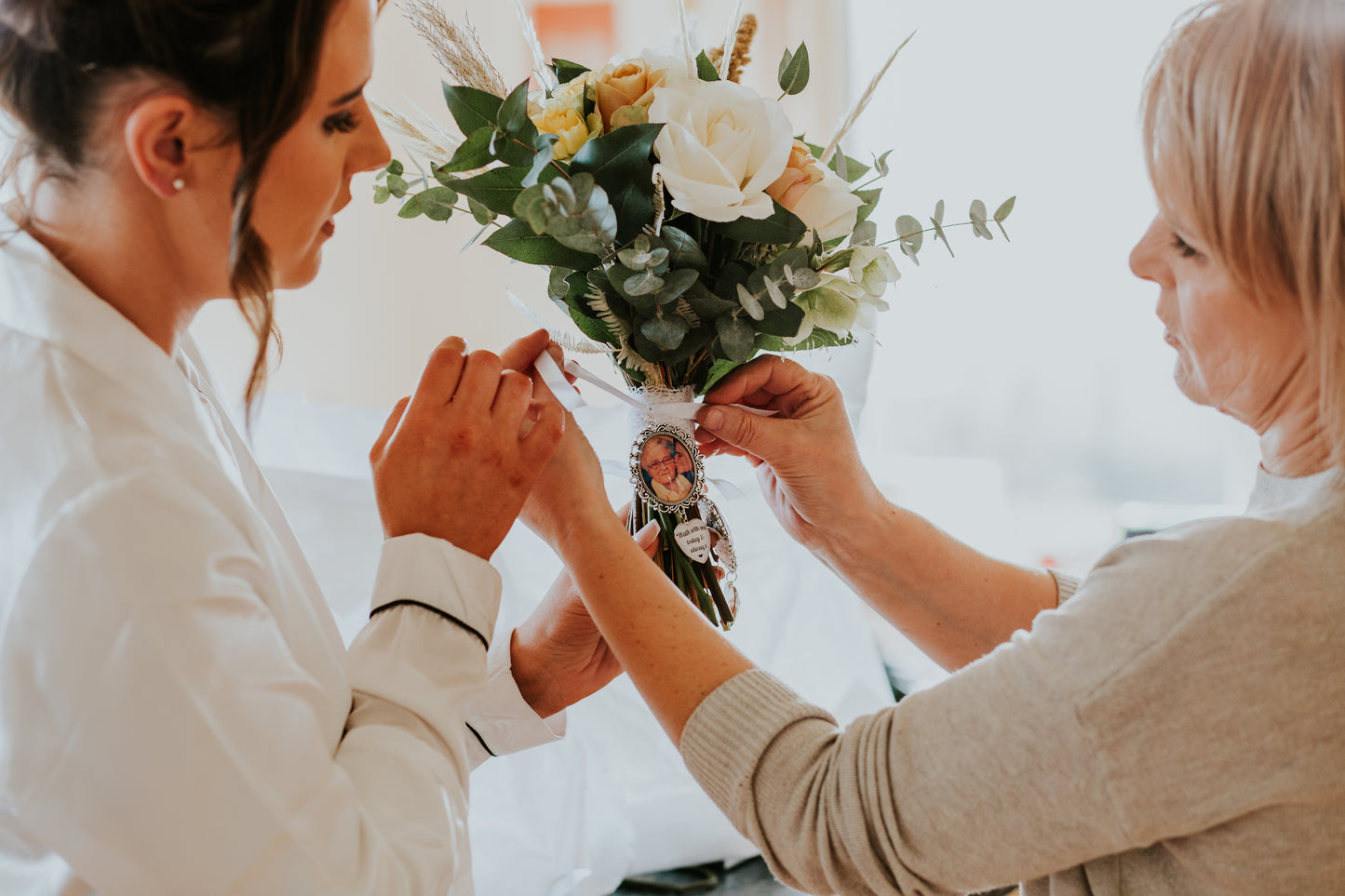 Two women holding hands with a bouquet of flowers and a photo inside one of the hands.