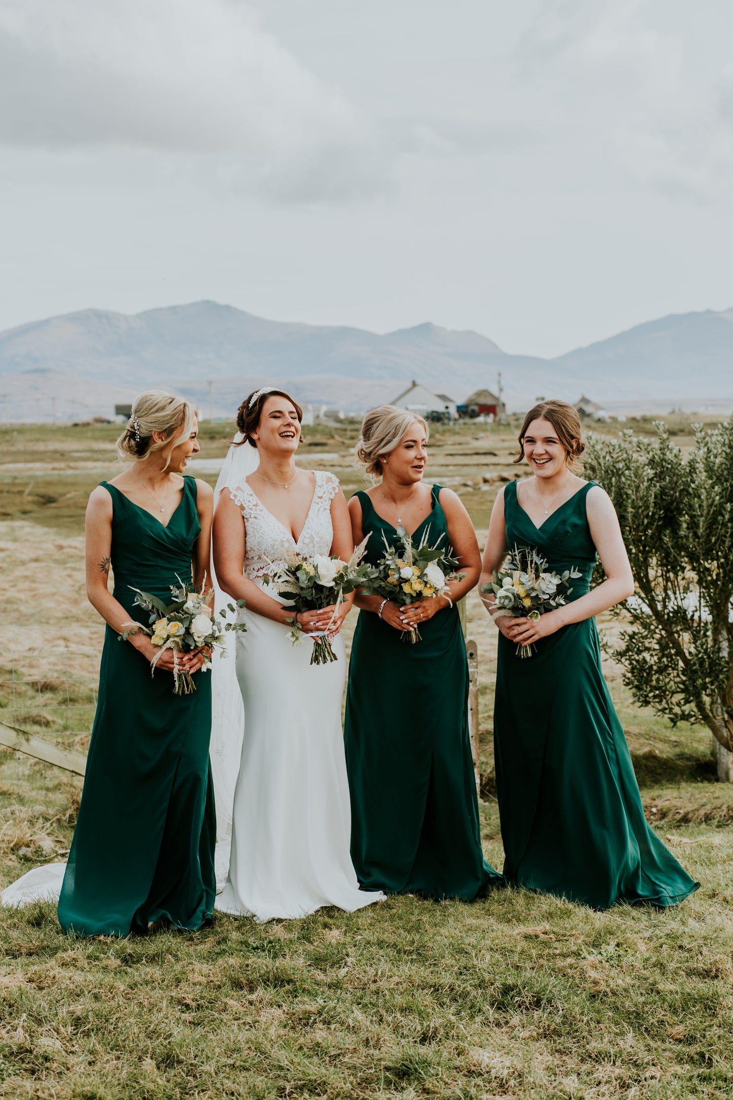 Bride and three bridesmaids in green dresses standing outdoors with mountains in the background