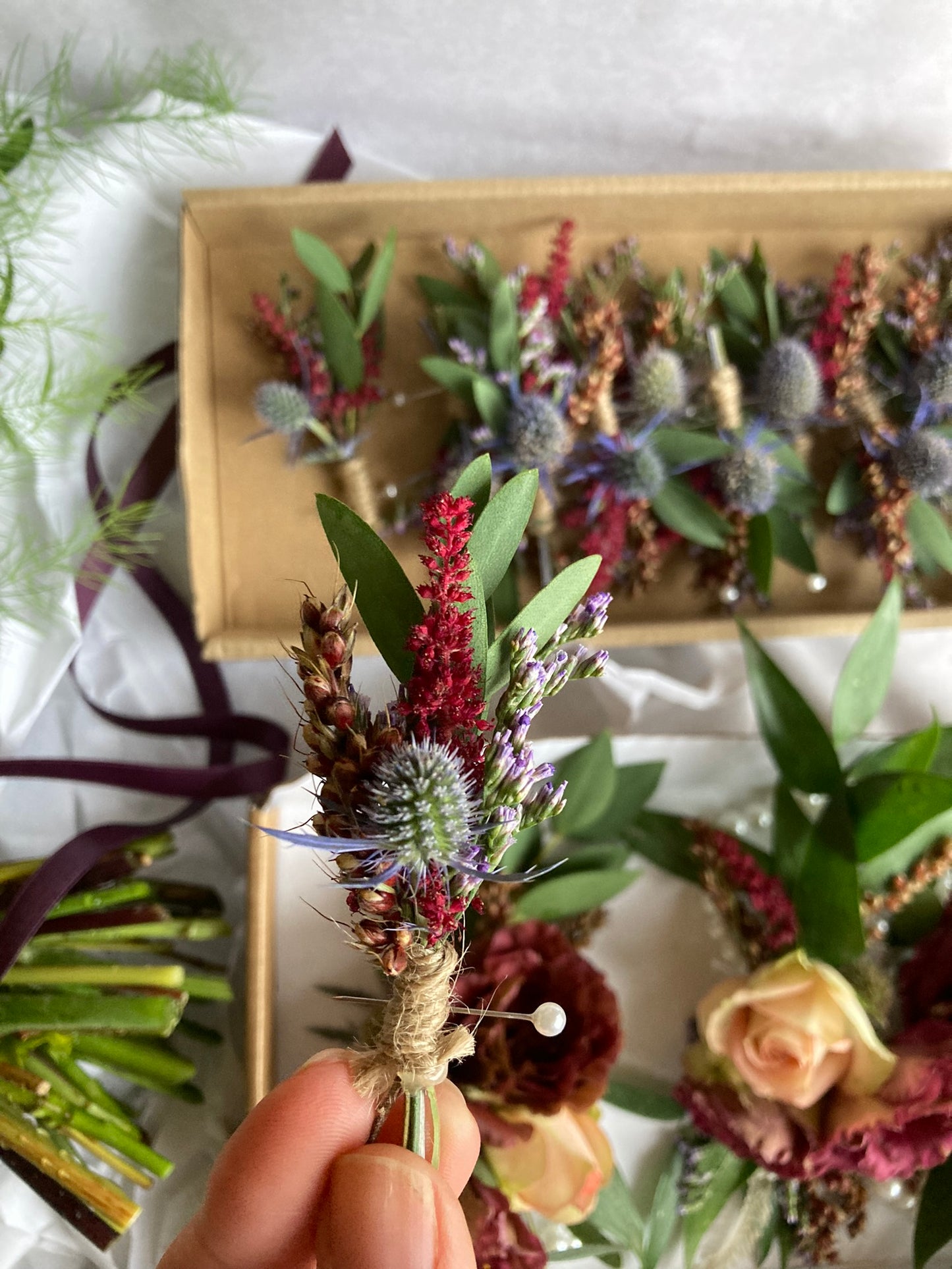 Hand holding a floral boutonniere with a display of more boutonnieres in the background.