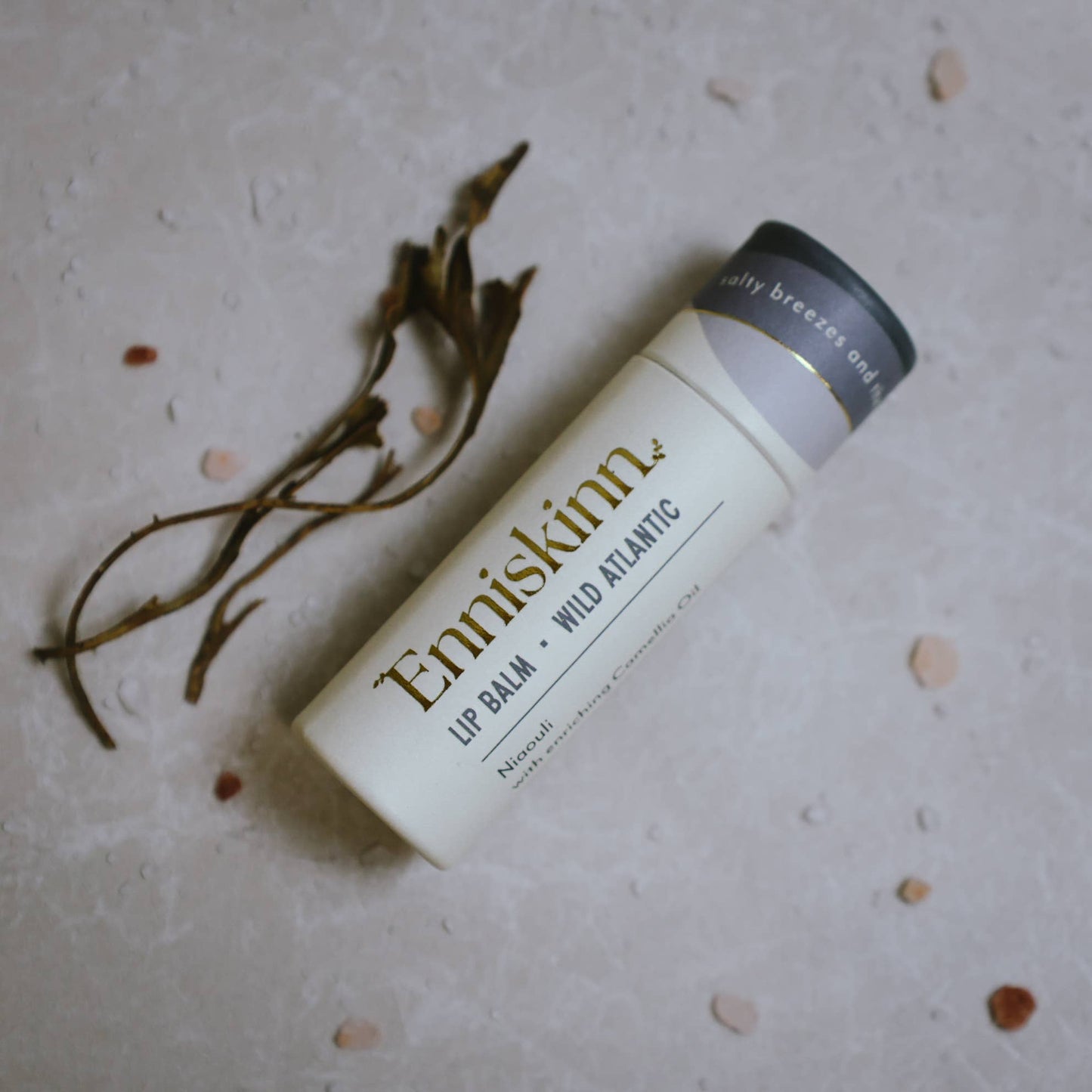 Enniskinn lip balm on a textured surface with dried plants