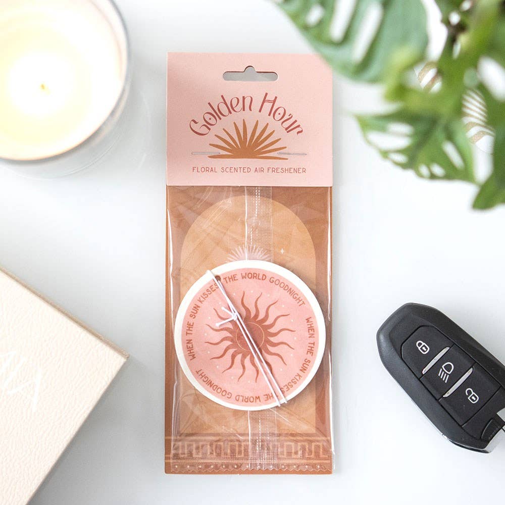 Packaged Golden Hour floral scented air freshener with a car key and candle in the background.