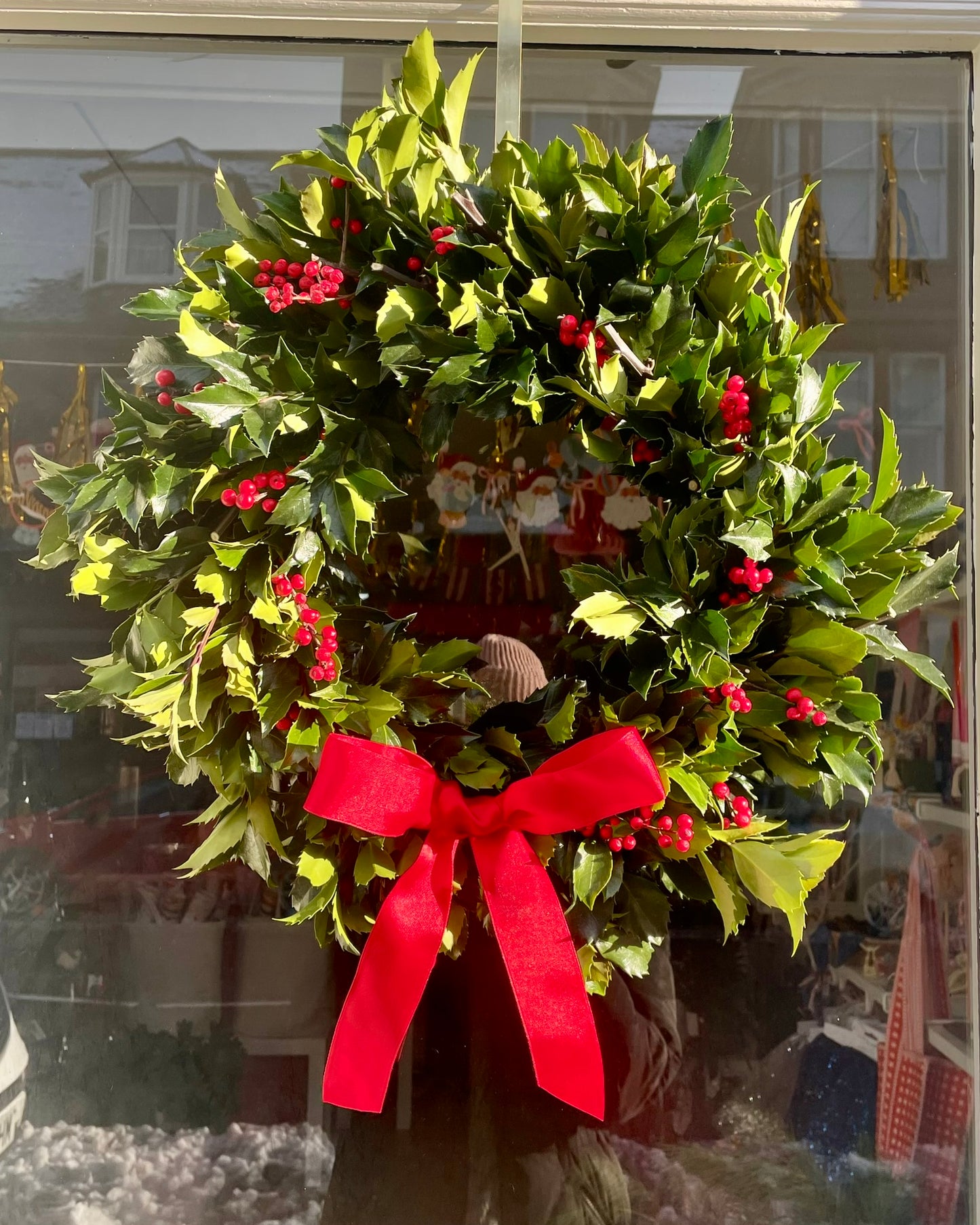 Christmas wreath with holly leaves and red berries on a glass door.