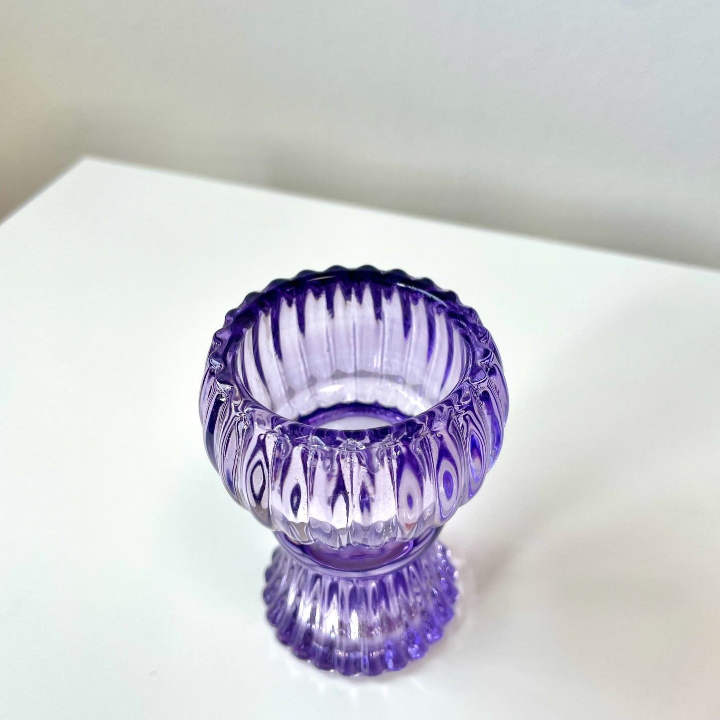 Purple glass candle holder on a white surface with a blurred background