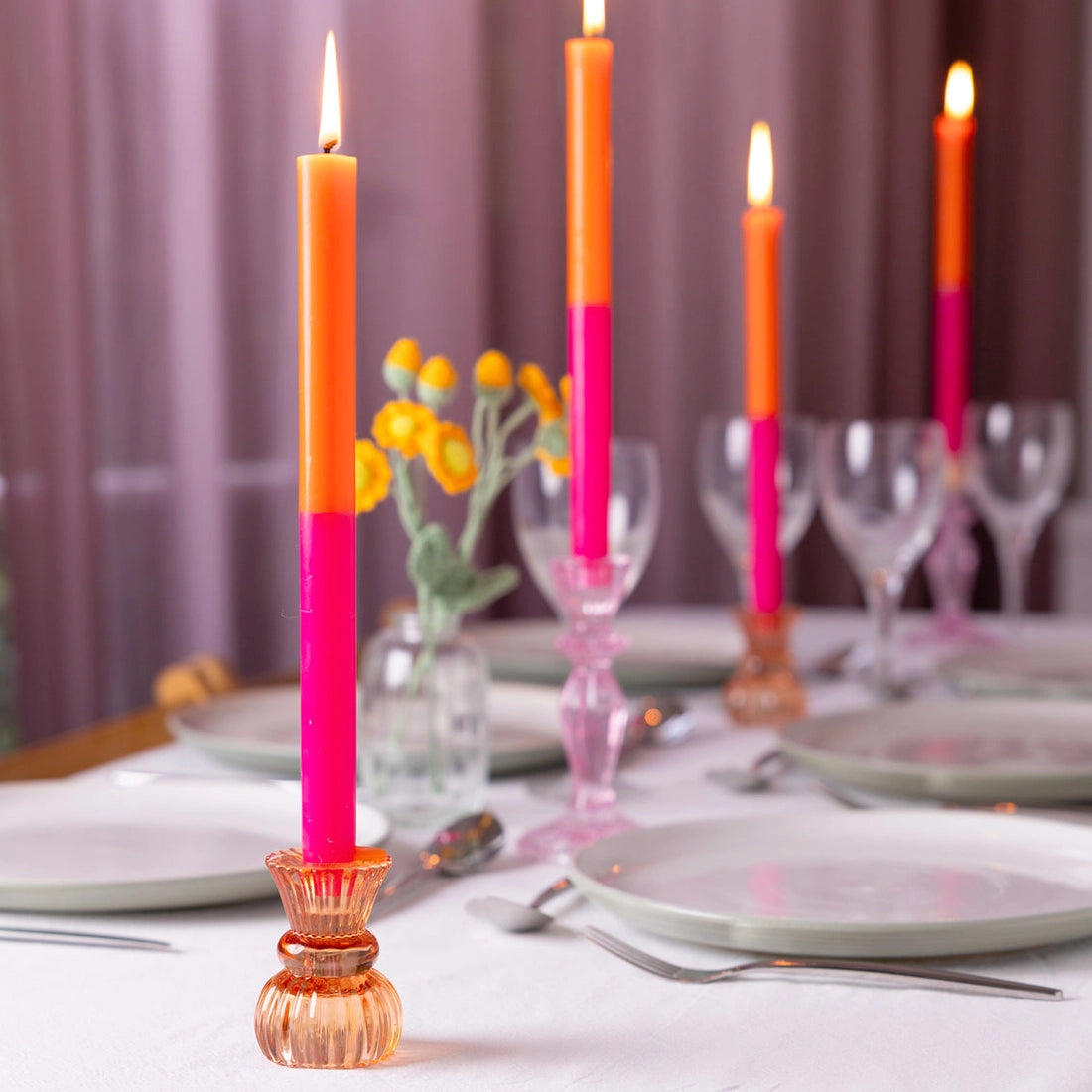 Colorful candles on a table setting with plates, cutlery, and glasses.