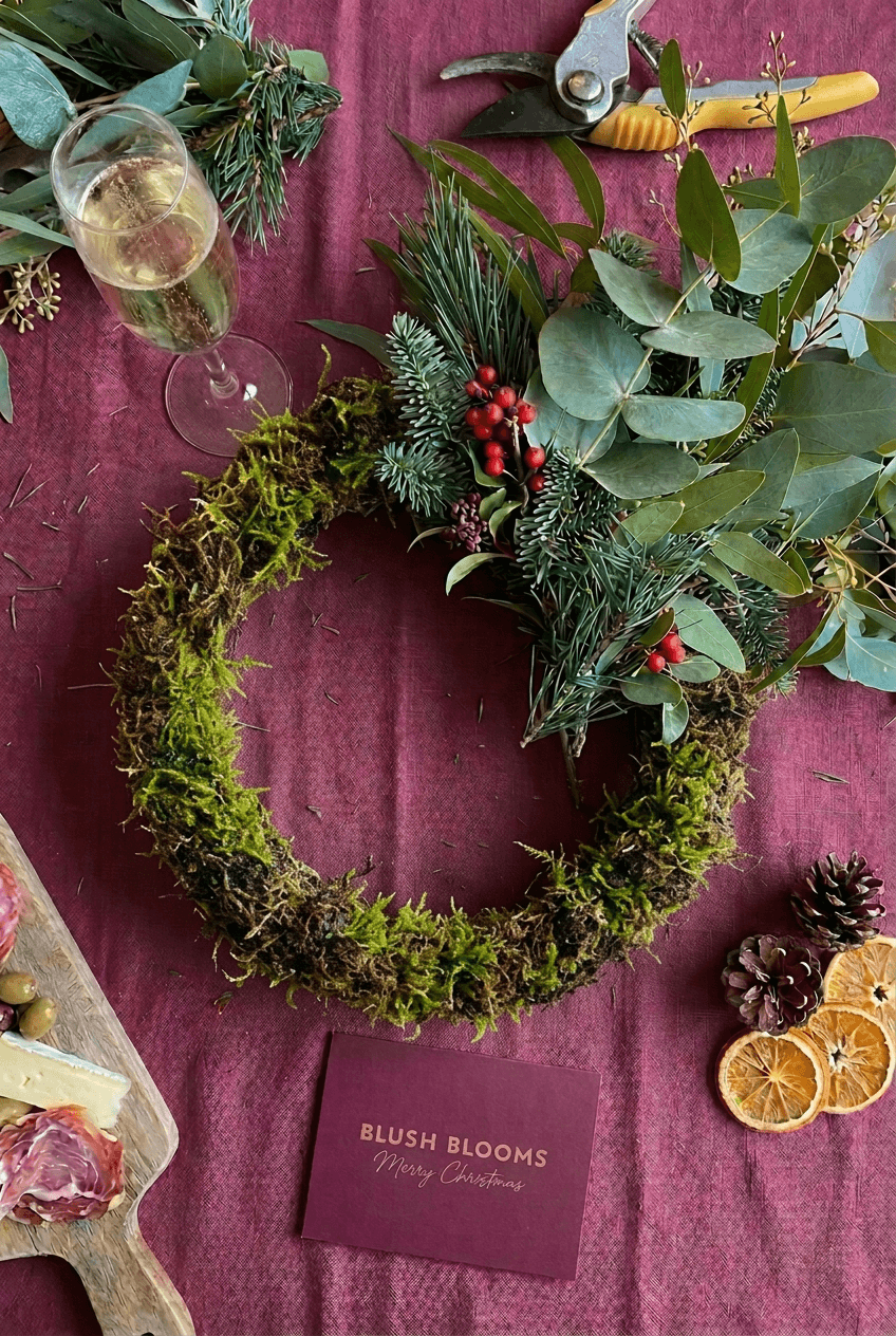 Traditional moss-based Christmas wreath in progress with seasonal foliage, florist tools and festive refreshments at Blush Blooms in Stonehaven.