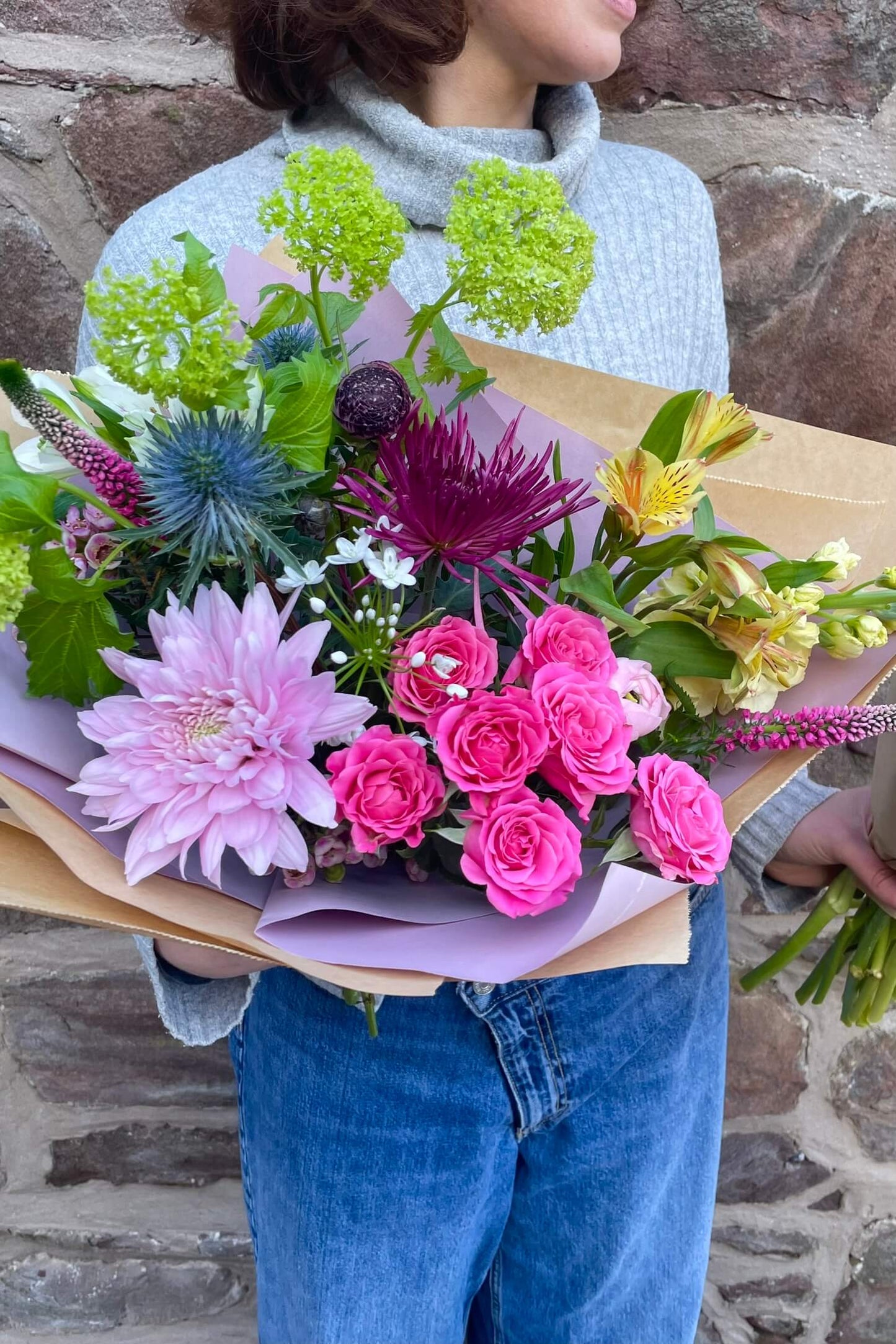 Dainty Mother’s Day Florist Choice bouquet by Blush Blooms, featuring pink spray roses, chrysanthemum, thistle and seasonal spring flowers, hand-tied and wrapped in lilac and kraft paper