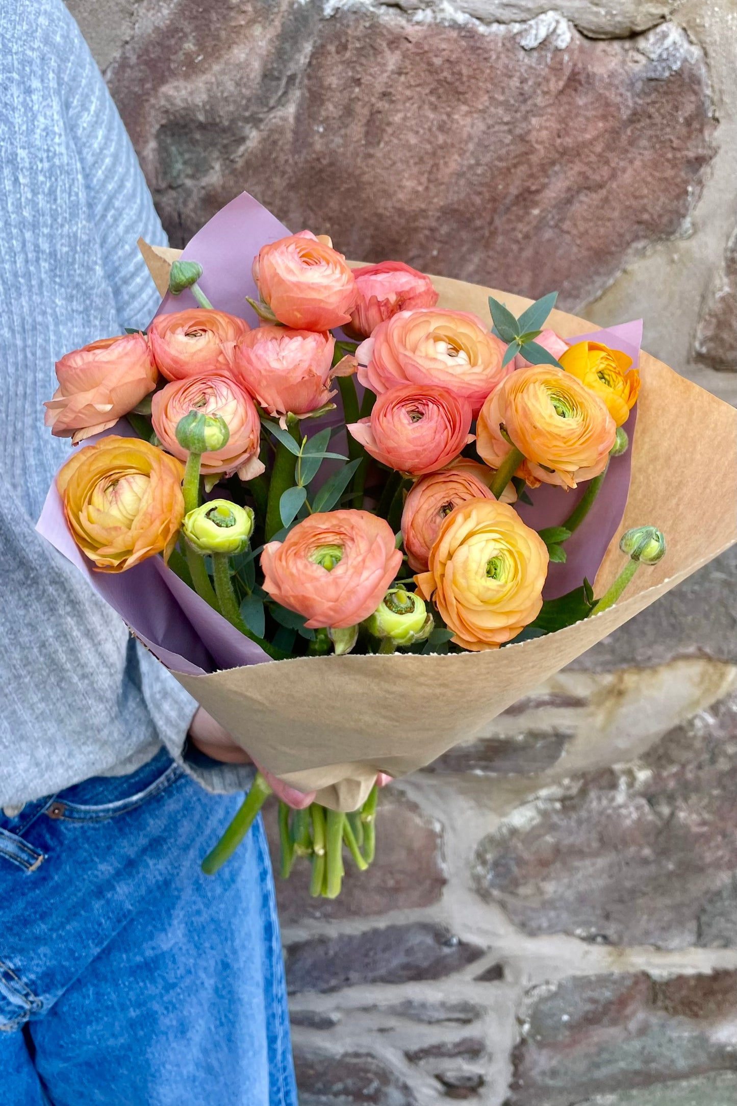 Seasonal ranunculus stems in peach and orange tones, hand-wrapped in paper