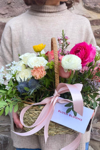 The Spring Basket with roses, ranunculus and tulips arranged in a woven basket with a blush ribbon.